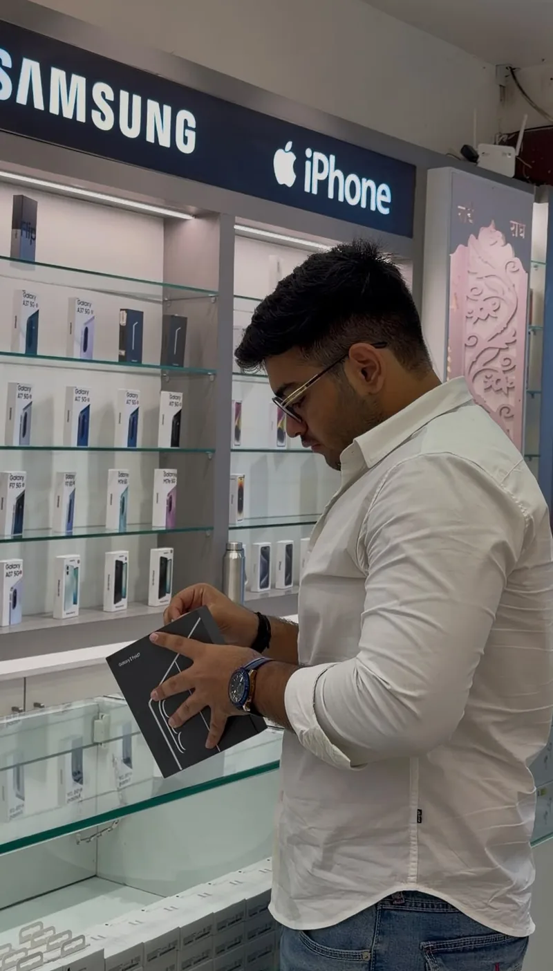 A customer inspecting a new Samsung Galaxy Z Fold box in front of the Samsung and iPhone display wall.